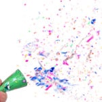 Hand firing off confetti.  Focus is on the cone.  Confetti is blurry due to motion